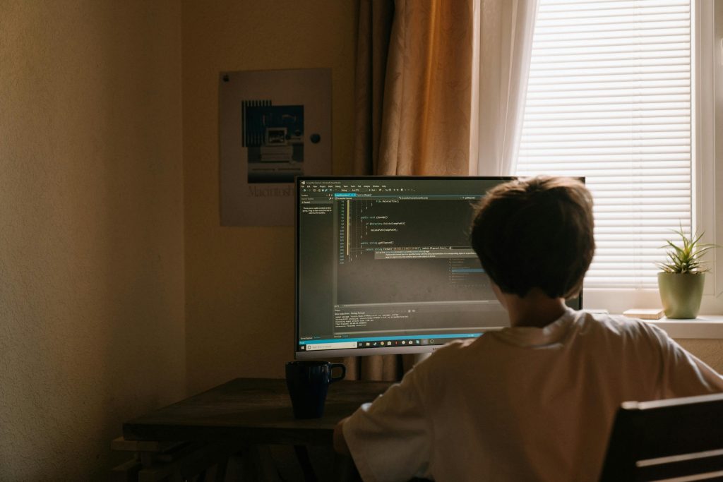 A young person focused on computer programming at a home desk. Cozy and tech-centric environment.